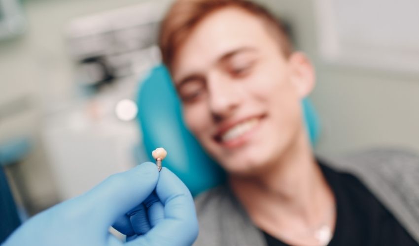 Diş hekimi, gülümseyen genç hastasına diş implantı örneği gösteriyor.