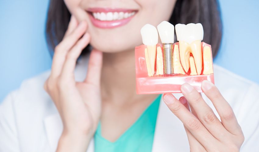 Diş implantı tedavisini anlatan kadın hekim, implant modeli tutuyor.