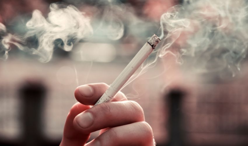 Sigara içen bir kişi ve yükselen duman, diş implantı sağlığına zarar verebilir.